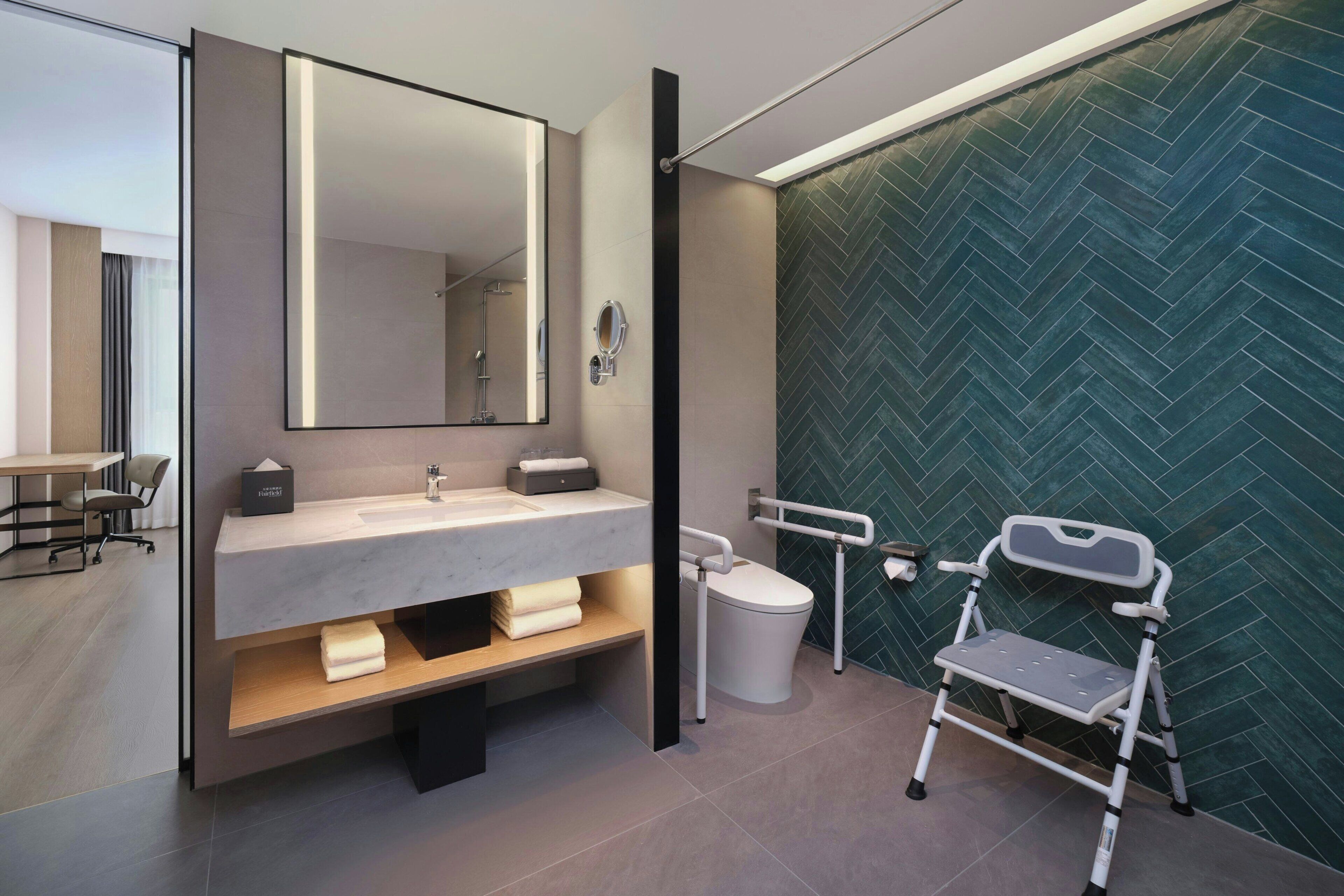A modern bathroom with a large mirror, a sink, a toilet, and a wheelchair-accessible bench.