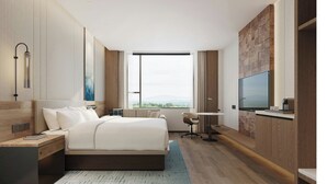 Ein modernes Hotelzimmer mit einem großen Bett, einem Schreibtisch, einem Fernseher und Blick ins Freie.