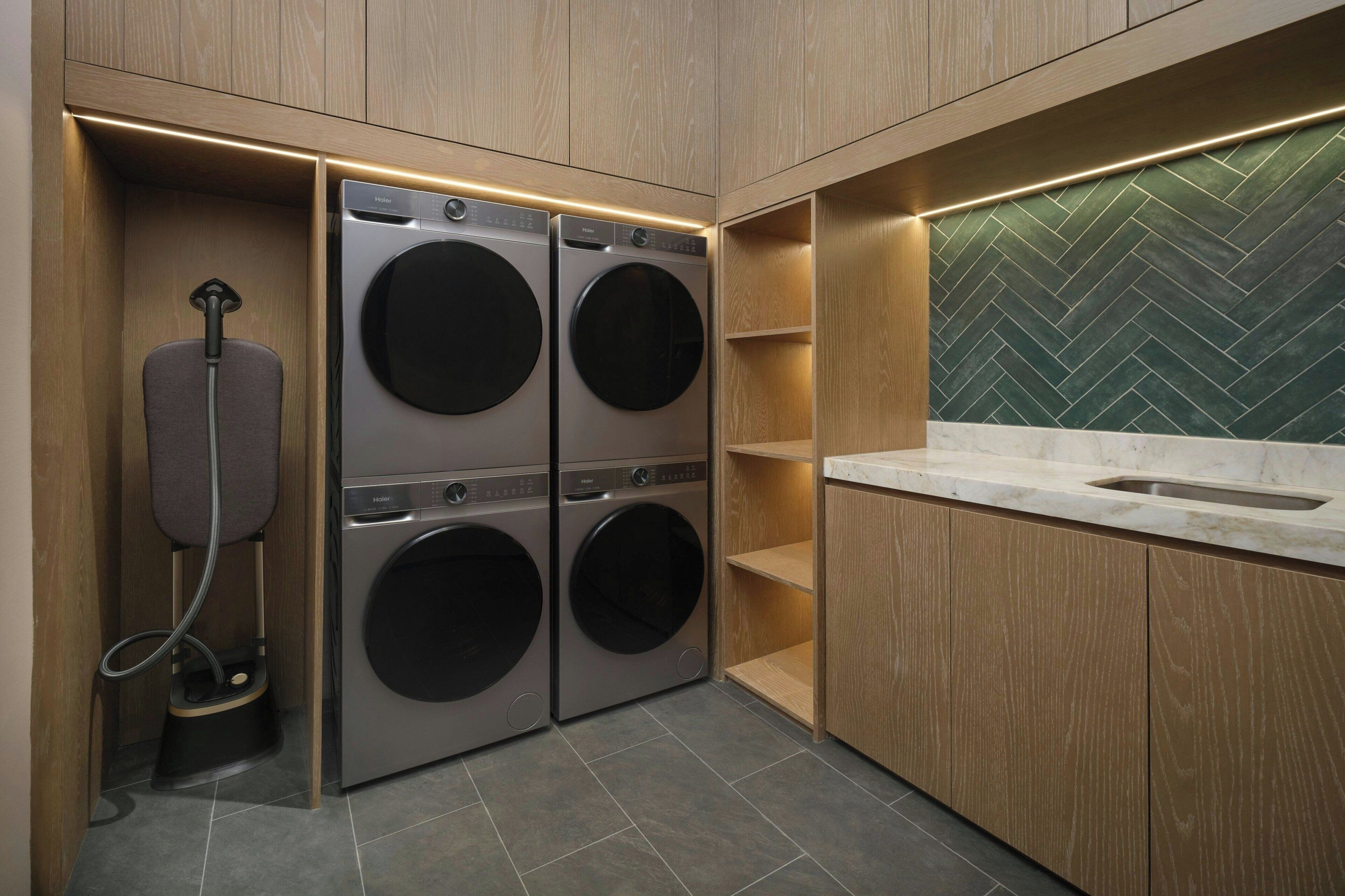 A compact laundry area with two front-loading washing machines, a built-in shoe dryer, and a herringbone-patterned backsplash.