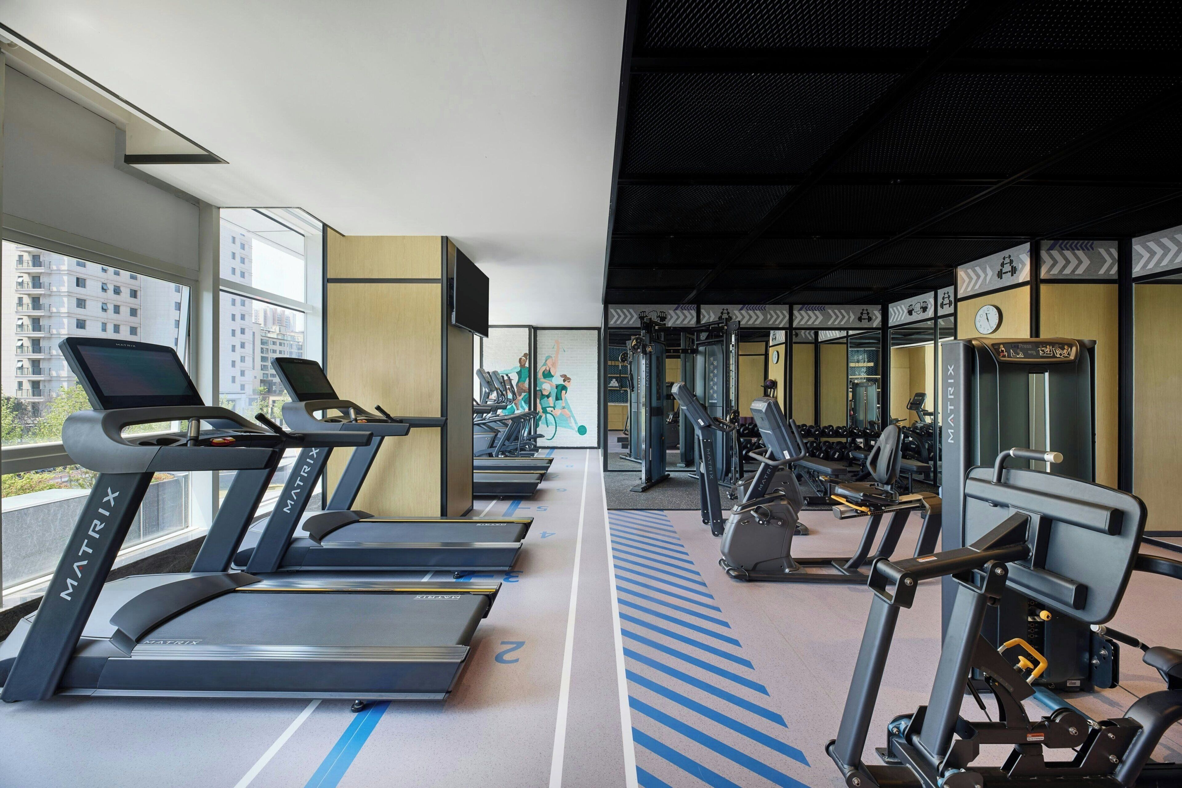 A gym with treadmills, weight machines, and a mirrored wall.