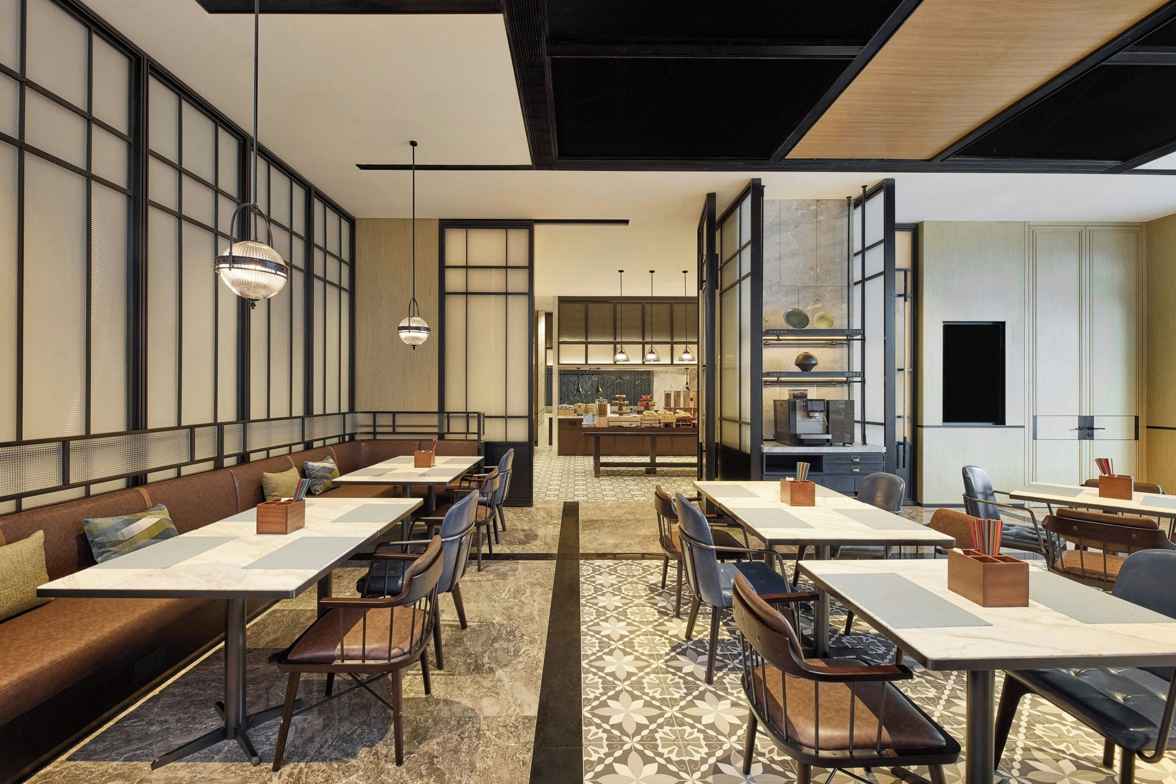 Un restaurante moderno con mesas altas y cabinas, una cocina al fondo y un suelo estampado.