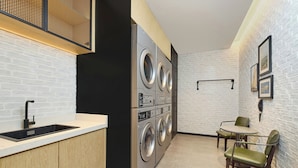 Une petite buanderie comprenant un évier, une machine à laver et un sèche-linge superposés, une petite table et des chaises.