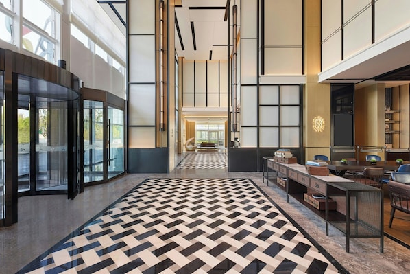 A spacious lobby with a geometric patterned floor, a reception desk, and a view of the cityscape through large windows. - Four Points By Sheraton Rizhao Central Activities Zone (Rizhao)