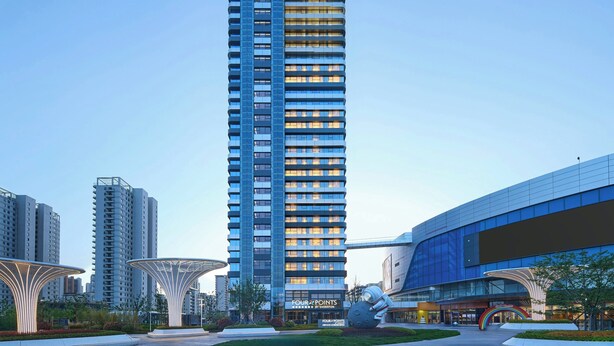 Ein hoch aufragendes Hotel mit modernem Design, das einen markanten Eingang und eine große, beleuchtete Skulptur zeigt.