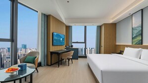 Une chambre d’hôtel équipée d’un lit, d’un bureau, d’une chaise et d’une grande fenêtre donnant sur la ville.
