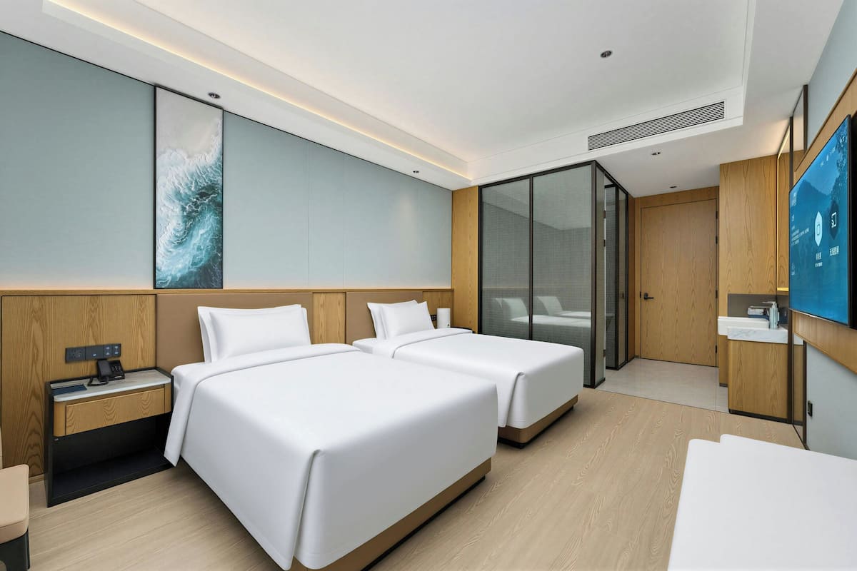 A hotel room with two beds, a TV, a desk, and a bathroom.