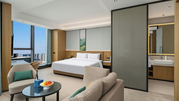 Une chambre d’hôtel moderne dotée d’un grand lit, d’un coin salon avec une table basse et un canapé, ainsi que d’une salle de bain avec un miroir et un lavabo.