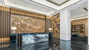 Un hall d’entrée avec un comptoir de réception en marbre, une grande fresque murale et une bibliothèque.