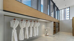 Une chambre d’hôtel moderne dotée d’une grande fenêtre, d’un porte-peignoir avec plusieurs peignoirs, d’un lave-linge intégré et d’un design minimaliste.