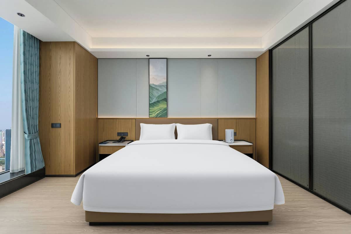A modern hotel room with a large bed, wooden paneling, a city view, and a large window with curtains.