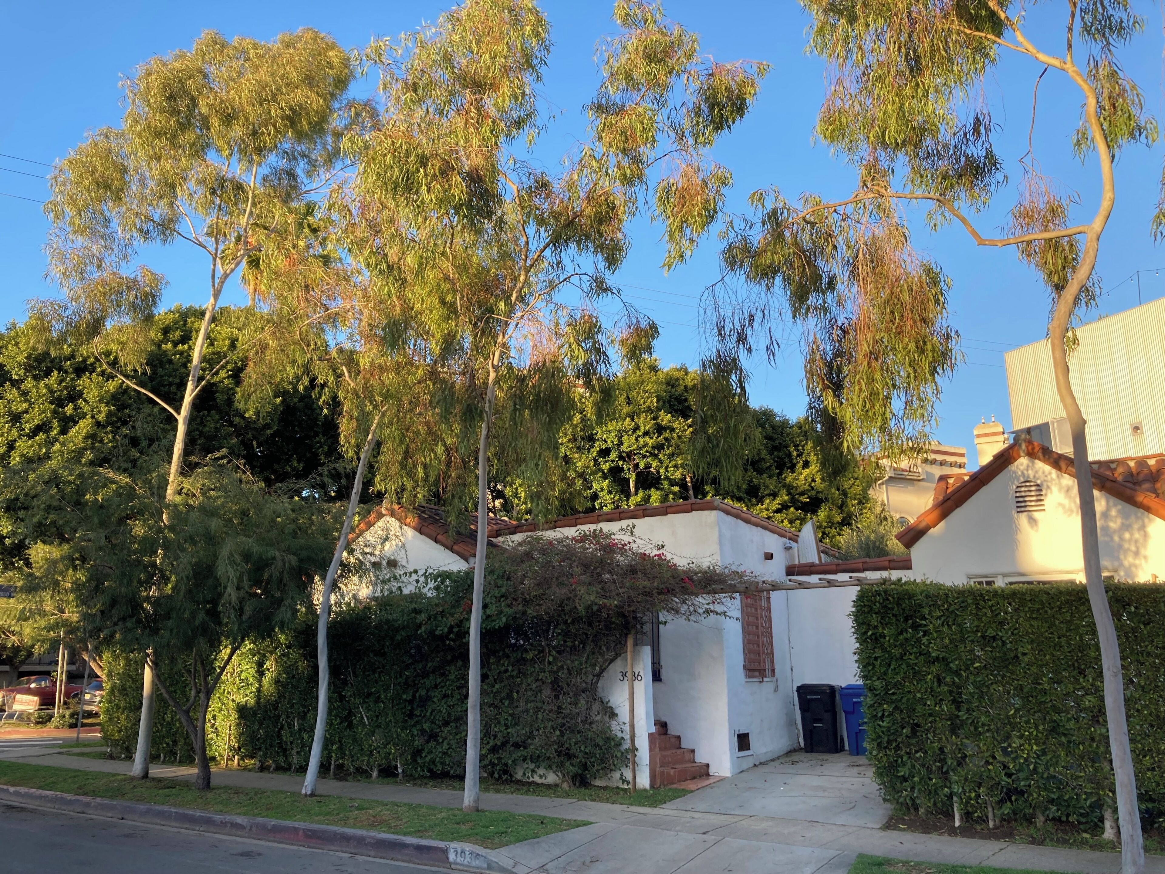 Um bairro residencial com uma casa branca, céu claro e uma rua.