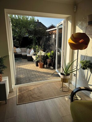 A room with a sliding glass door leading to an outdoor patio area with a sofa, potted plants, and a metal lamp. - House - Sleeps 6 - Private Garden & Parking (Wokingham)