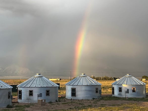 Una fila de silos metálicos de grano con un arcoíris al fondo.