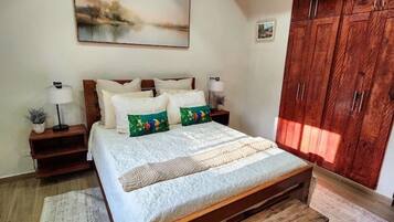 A bedroom with a wooden bed, a bench, a nightstand with a lamp, and a wardrobe.