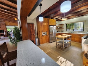 A modern kitchen with wooden cabinets, a stainless steel refrigerator, and a dining area with a table and chairs.