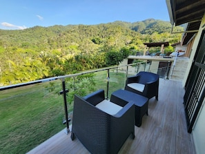 Ein Balkon mit Korbmöbeln, der einen üppigen grünen Landschaftsbereich und Berge blickt.
