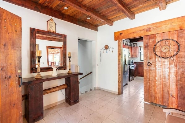 Interior em madeira com escada, cozinha visível através de uma porta aberta e um espelho decorativo.