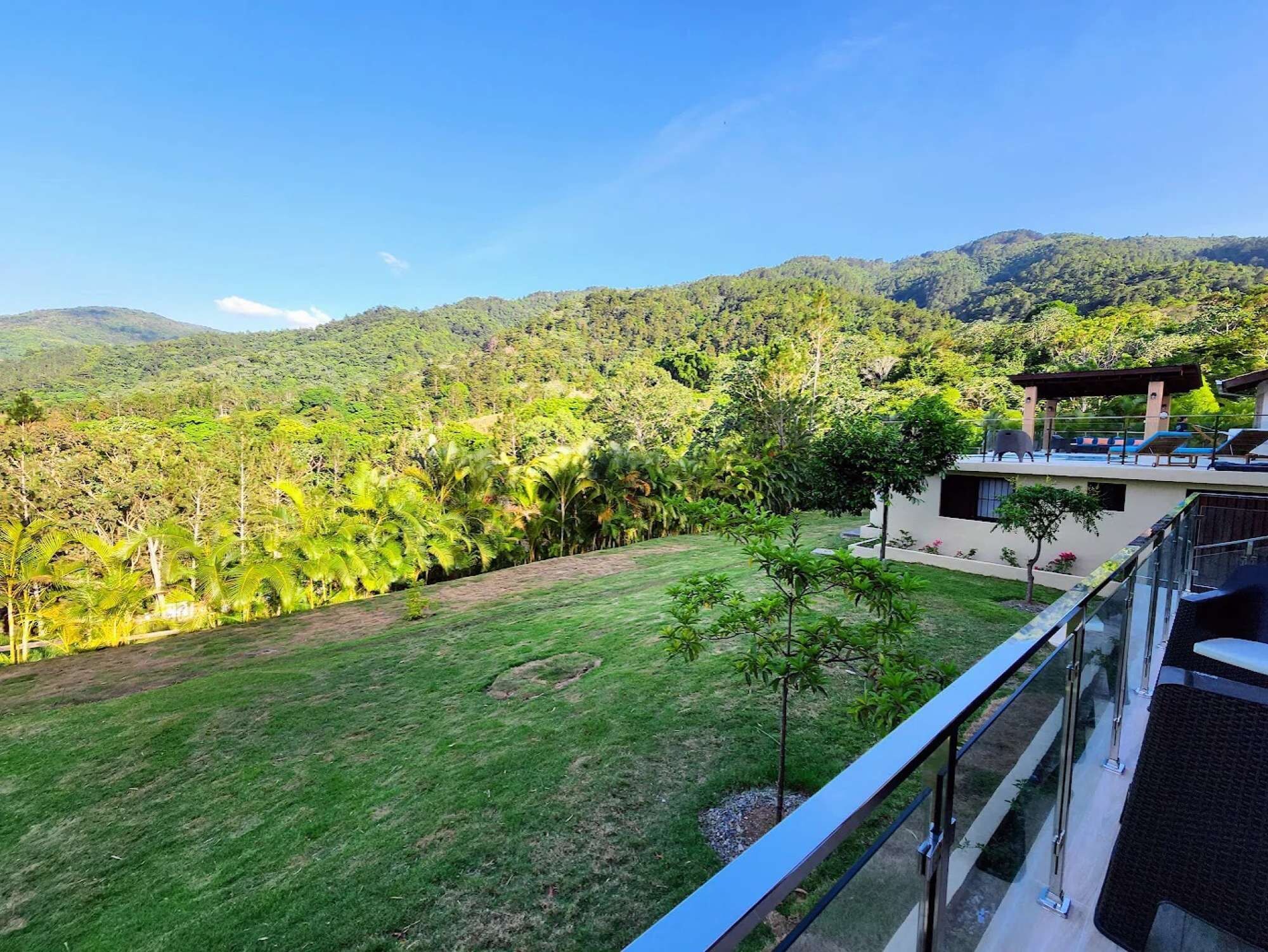 A modern building with a glass balcony overlooking a lush green landscape and mountains.