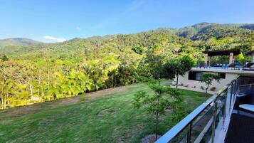 A modern building with a glass balcony overlooking a lush green landscape and mountains.