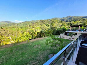 Un edificio moderno con un balcón de vidrio que da a un exuberante paisaje verde y montañas.