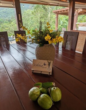 A wooden table with a woven vase of yellow flowers, a welcome sign, and green fruits.