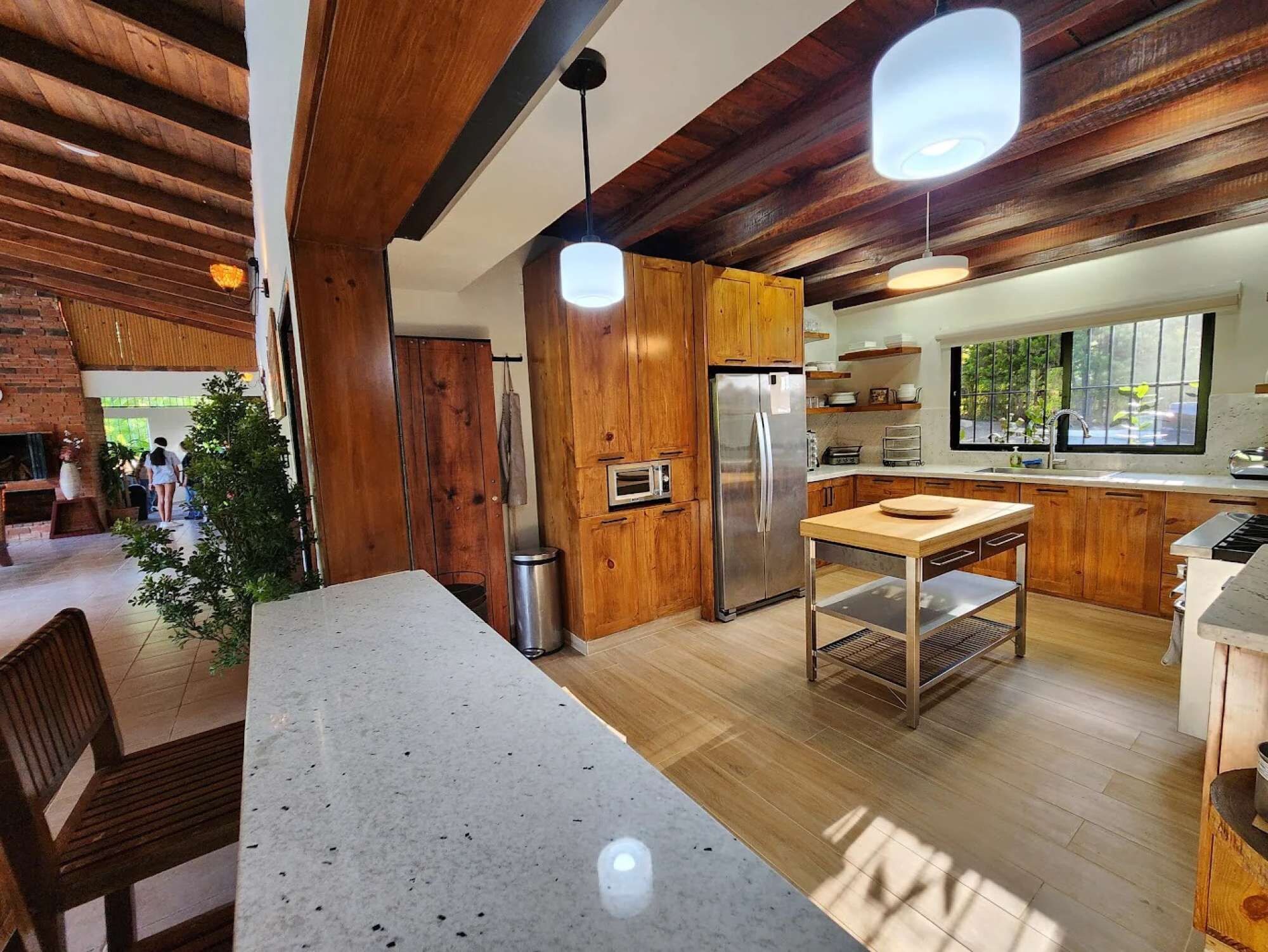 A modern kitchen with wooden cabinets, a stainless steel refrigerator, and a dining area with a table and chairs.