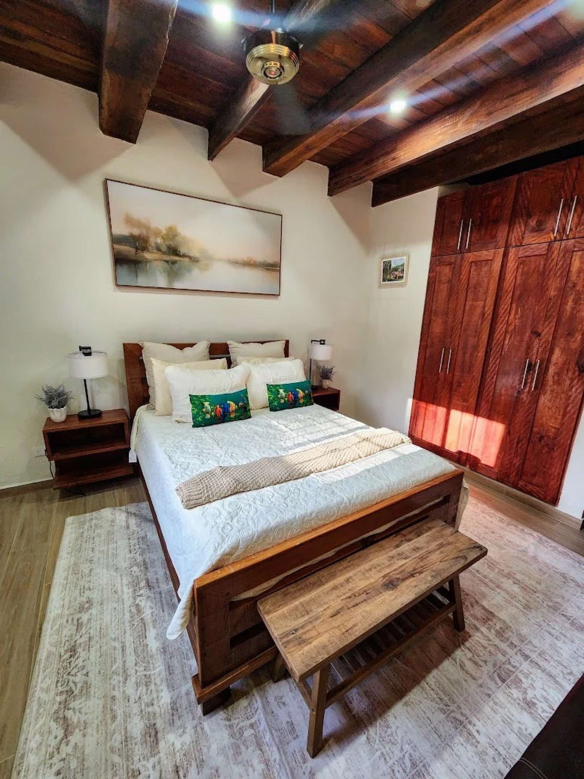 A bedroom with a wooden bed, a bench, a nightstand with a lamp, and a wardrobe.