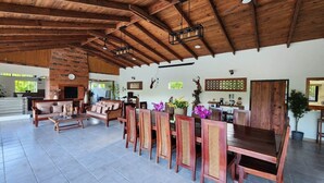 A spacious living area with a high ceiling, wooden beams, a fireplace, and a dining area with wooden chairs and a table.