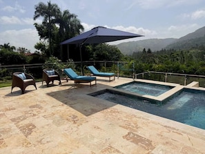 Zona de piscina con sillones de descanso y un gran paraguas.