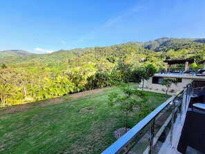 A modern building with a glass balcony overlooking a lush green landscape and mountains.