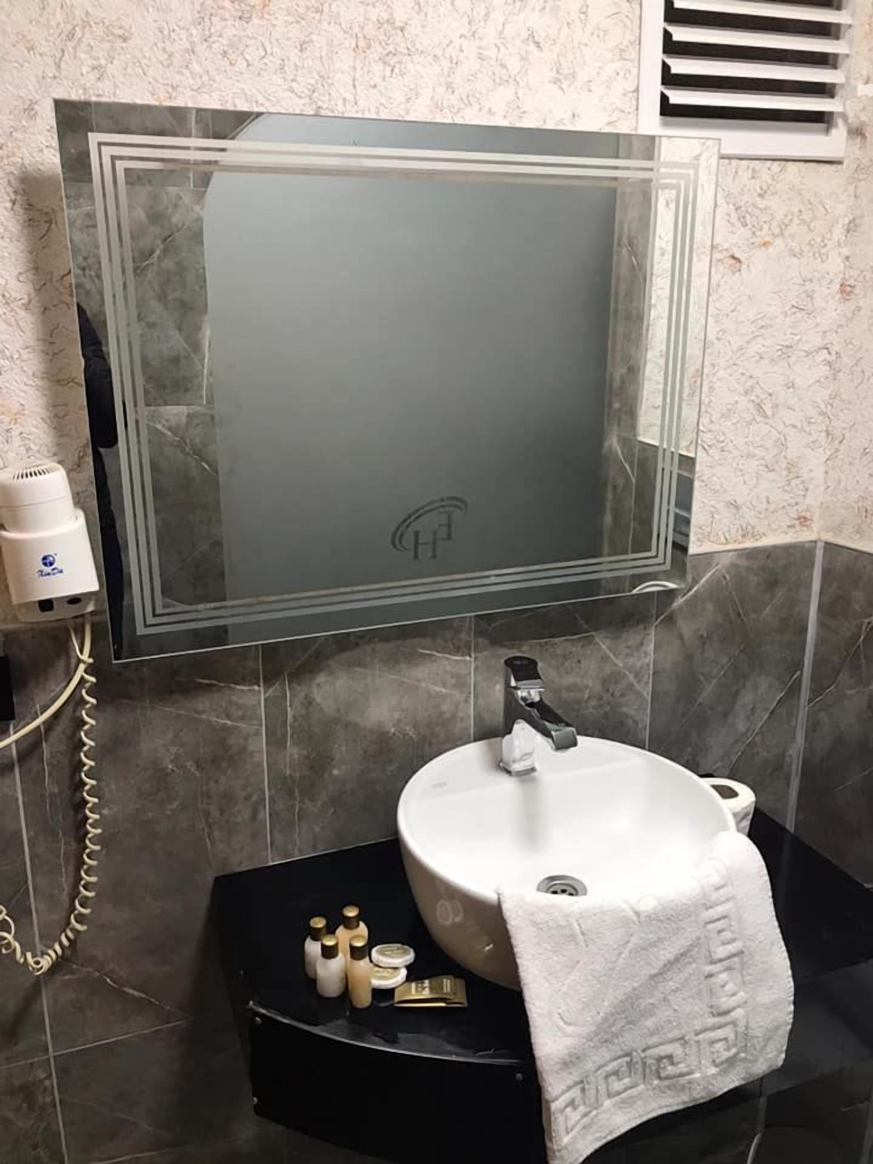 A bathroom with a large mirror, a white sink, and a black vanity.