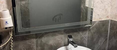 A bathroom with a large mirror, a white sink, and a black vanity.