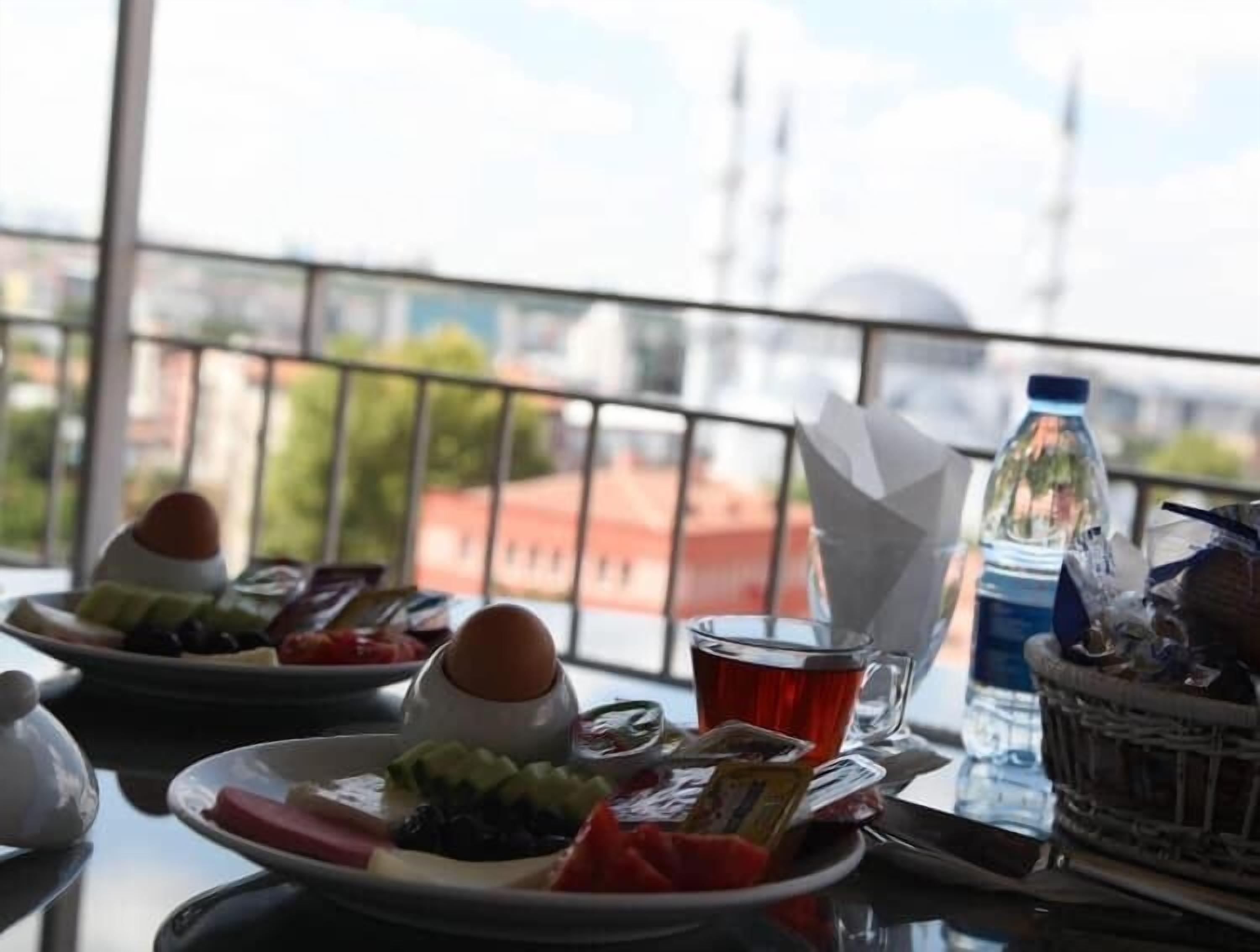A balcony with a table set for breakfast, including plates of food, a glass of tea, and a bottle of water.