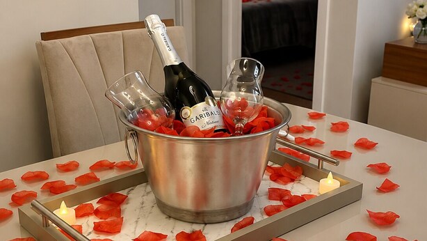 Een kamer met een bed, een nachtkastje met een bloevas, en een emmer met champagneflessen en glazen.