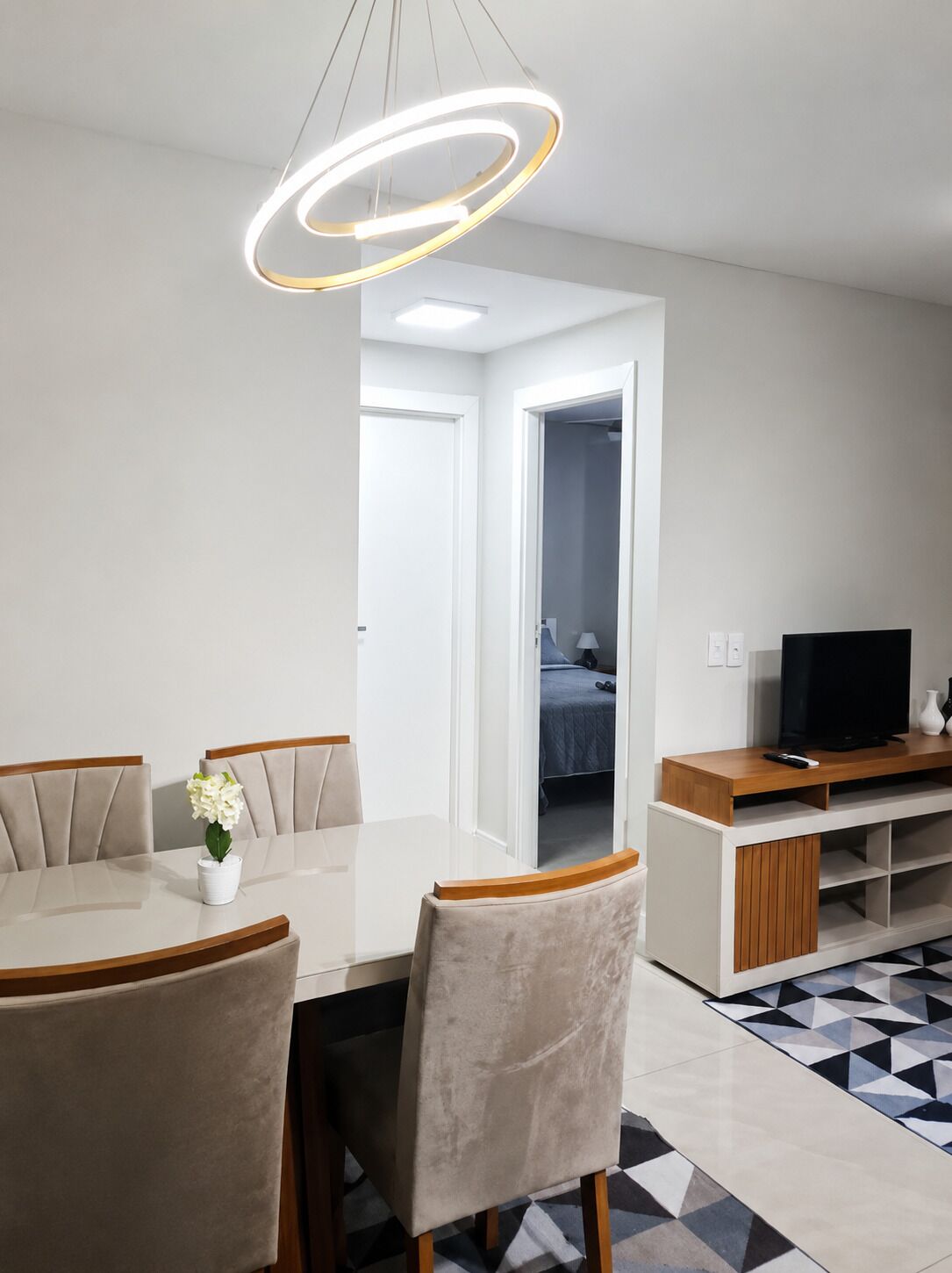 Una sala de estar moderna con una mesa de comedor, sillas, un televisor y un piso con un estampado geométrico.