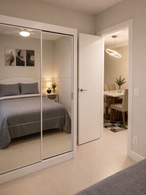 Une chambre à coucher comprenant un lit, une table de chevet avec une lampe, un miroir et une porte donnant sur un coin repas avec une table et des chaises.