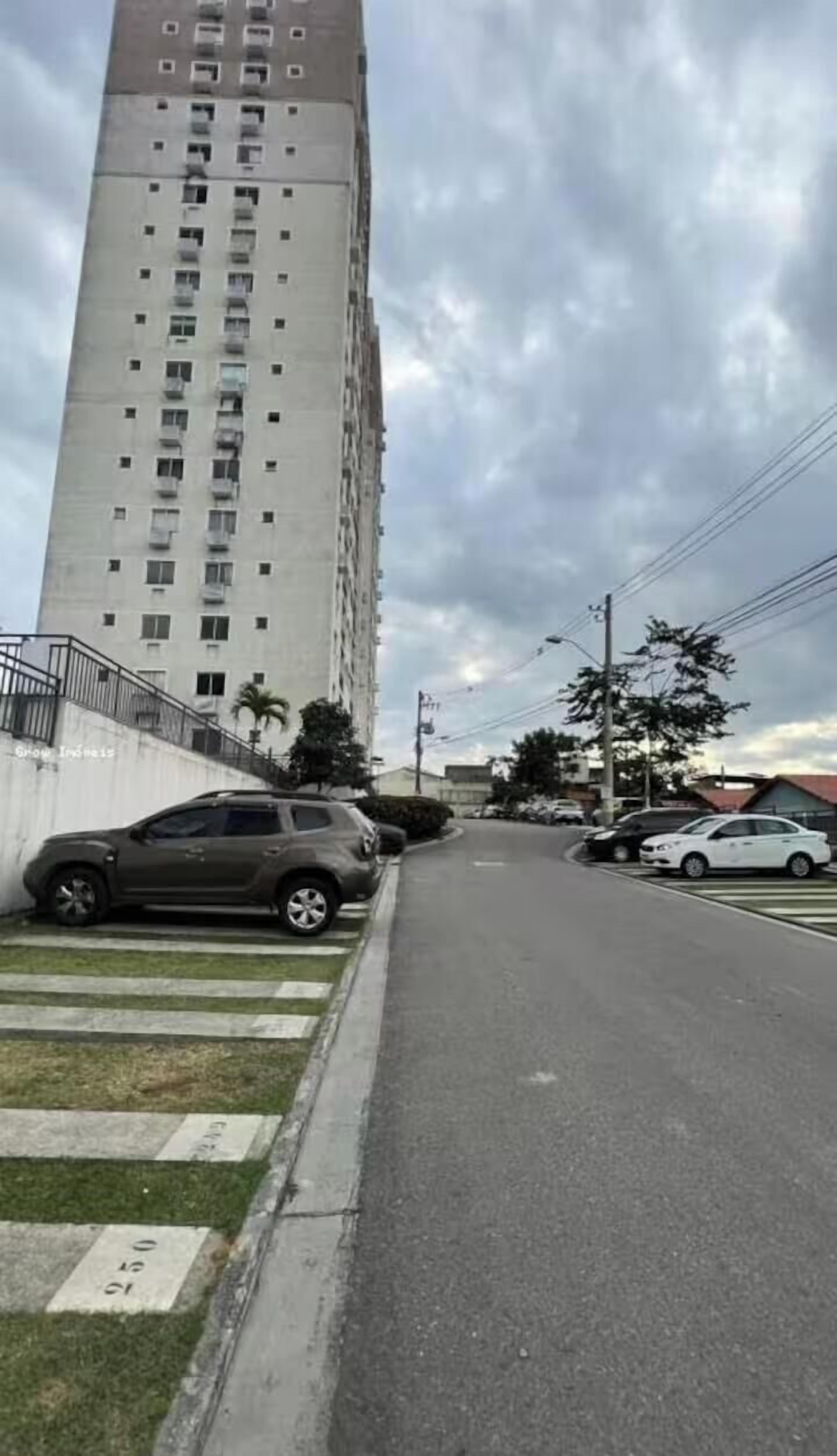 Un grand immeuble avec de nombreuses fenêtres, une zone herbeuse avec un passage piéton et des voitures garées le long de la rue.