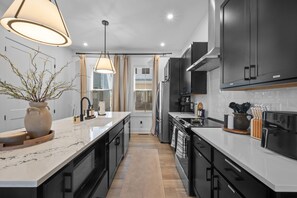 Una cocina moderna con encimeras de mármol, armarios negros e iluminación colgante.