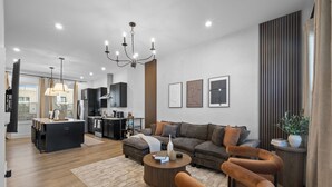 Een moderne woonkamer met een bank, fauteuils, een salontafel en een eethoek, met een keuken op de achtergrond.