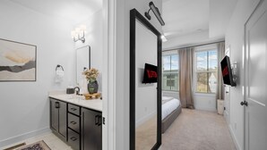 Een moderne slaapkamer met een groot bed, een inloopkast, een badkamer met een wastafel en spiegel, en uitzicht op het omliggende landschap.