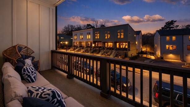 Een balkon met uitzicht op een woongebied in de schemering, een rieten stoel en een bank met decoratieve kussens.
