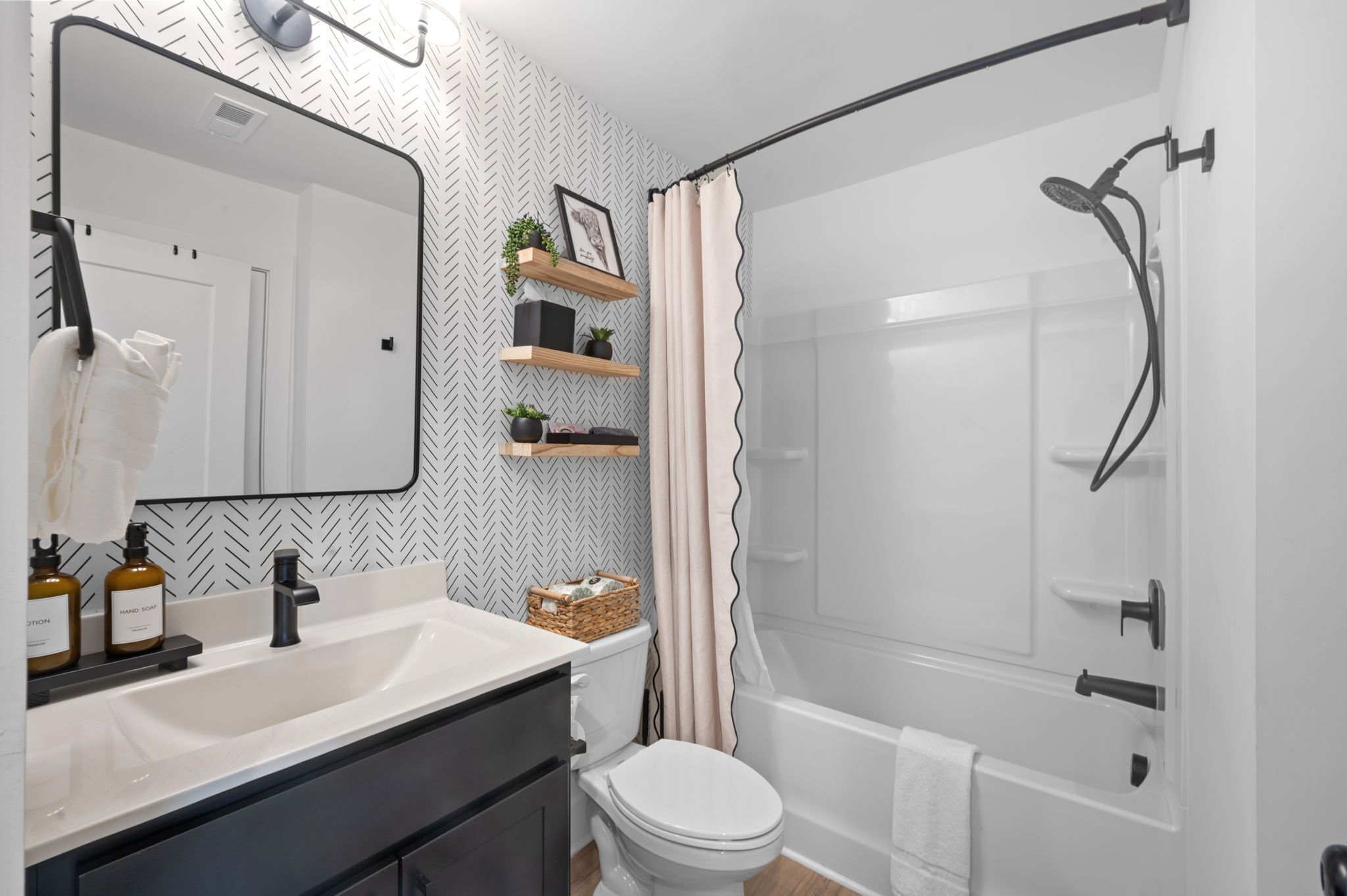 Une salle de bain avec un lavabo blanc, des toilettes, une douche avec une porte en verre et un miroir avec un cadre noir.