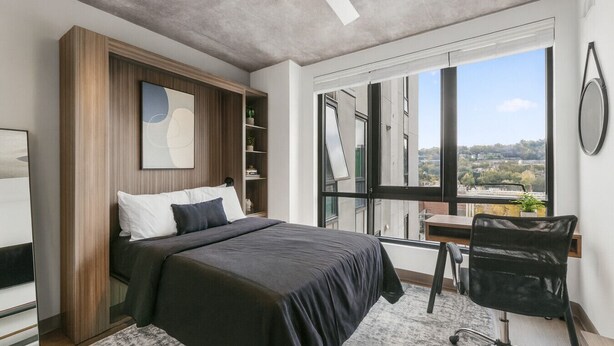 A modern bedroom with a large bed, a desk, and a chair. There is a window with a city view and a ceiling fan. - Cozy Murphy Hideaway Studio 18th (Birmingham)