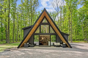 Una moderna baita con tetto a forma di triangolo, ampie finestre e vialetto in ghiaia.