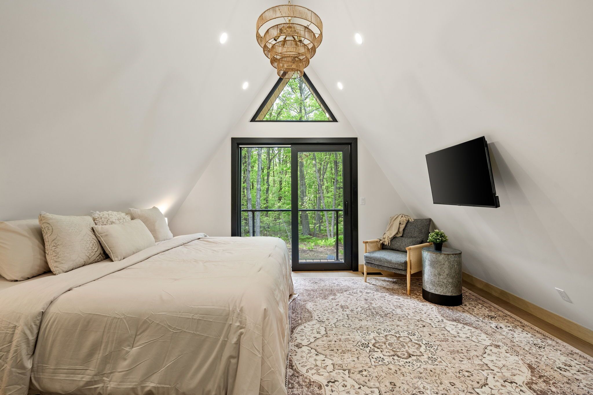 A bedroom with a bed, a large window, a television, and a small side table.