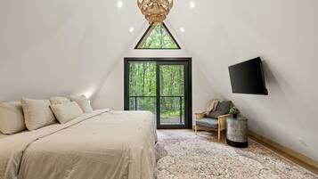 A bedroom with a bed, a large window, a television, and a small side table.