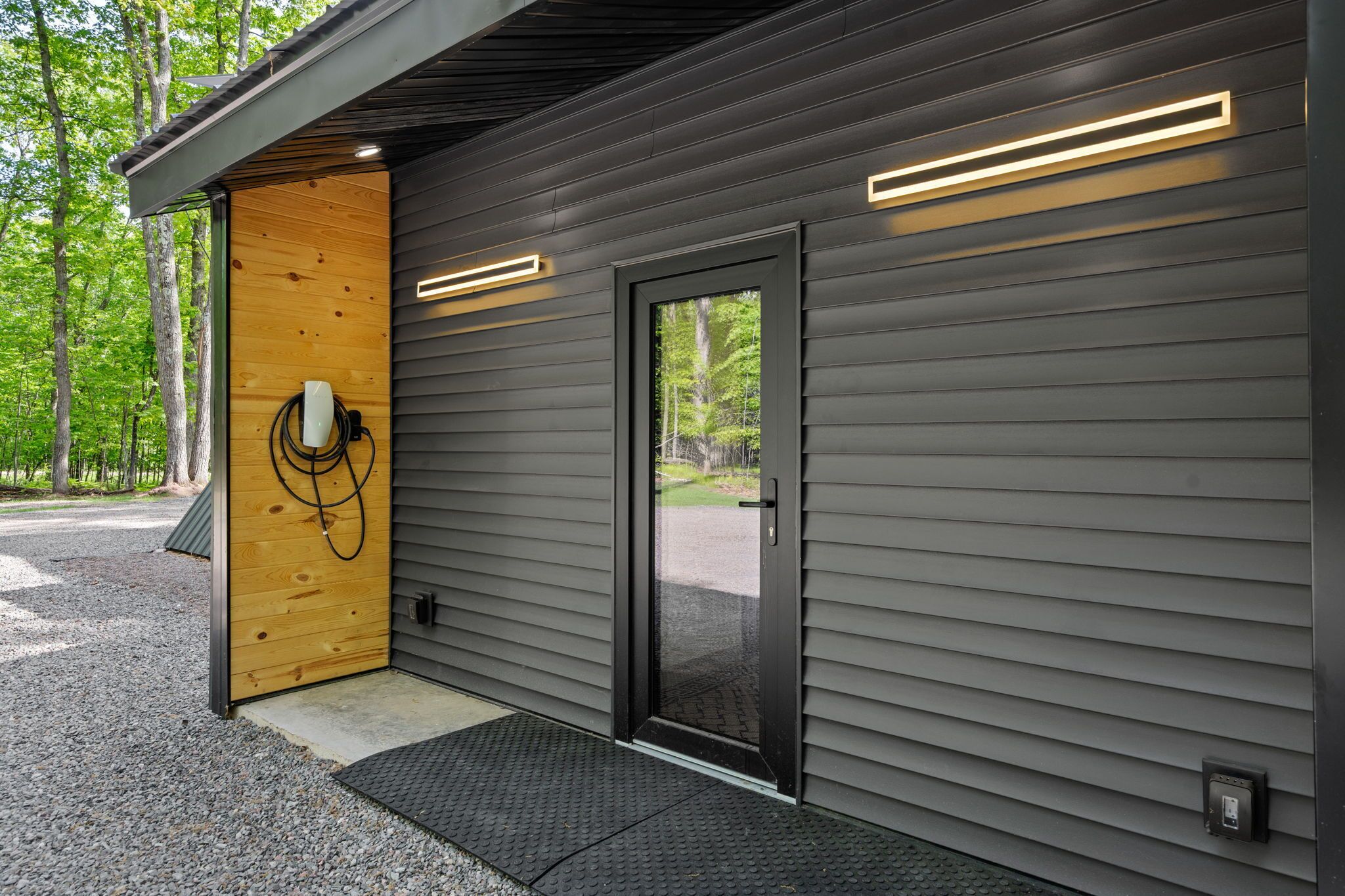 A modern building with a wooden door, a black sliding door, and a power outlet on the exterior wall.