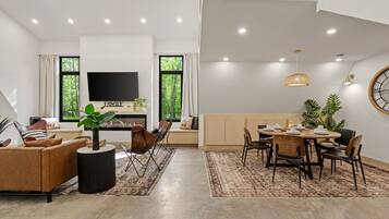 A modern living room with a sofa, TV, and dining area with chairs and a table.