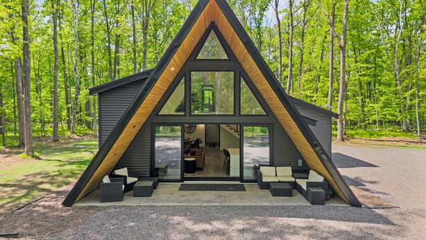 Una cabaña moderna con techo triangular, ventanas amplias y un patio con mobiliario.