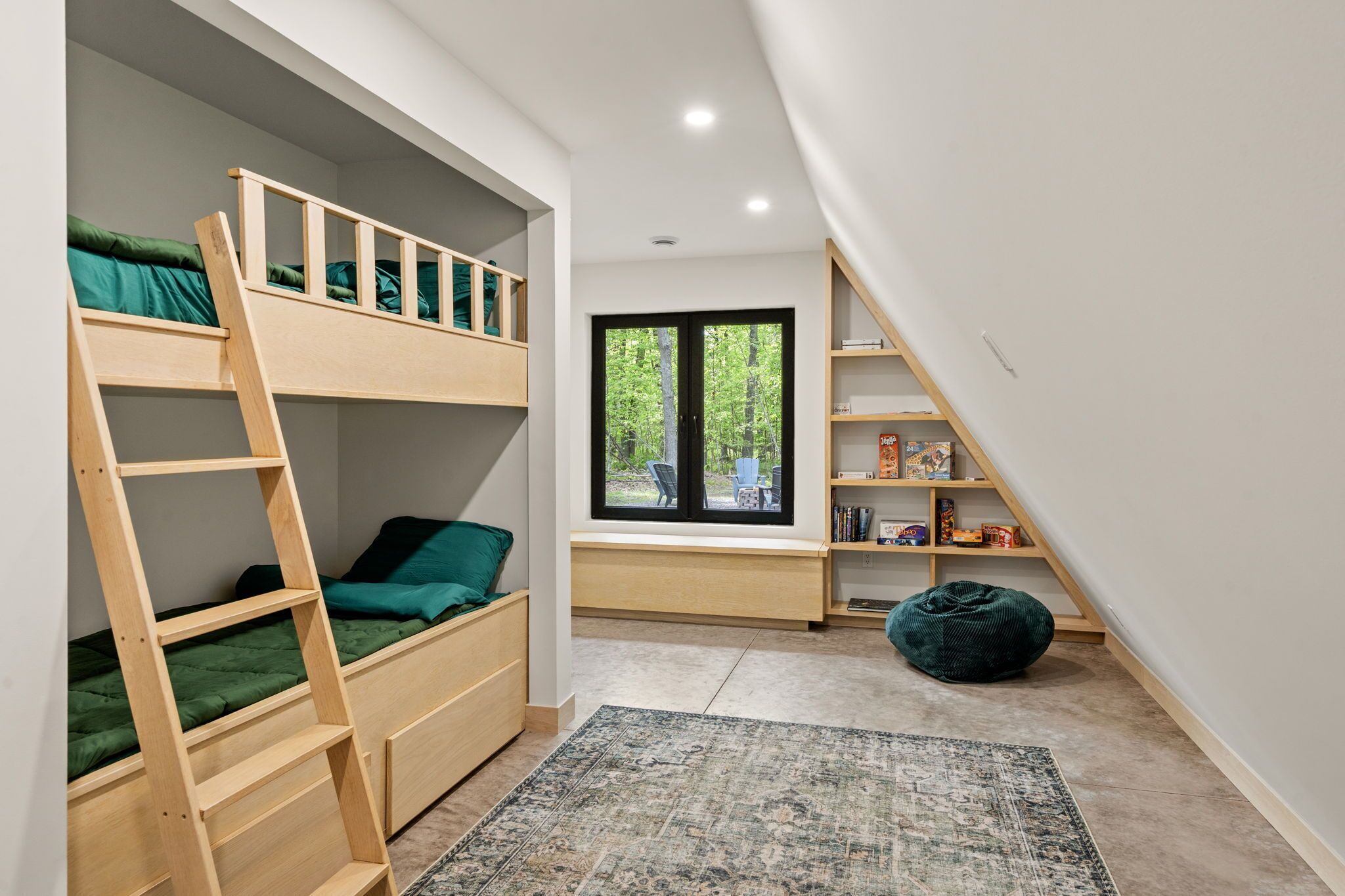 Une chambre avec un lit superposé, une fenêtre donnant sur un espace verdoyant, une bibliothèque et un fauteuil poire.